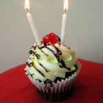 A cupcake with a cherry and two candles sits on a red felt table to help celebrate the Guelph Community Acupuncture birthday.