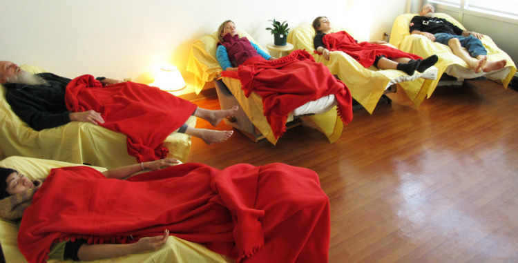 Five people sleeping during acupuncture treatment, covered in red blankets, lying in recliners arranged in a semi-circle.